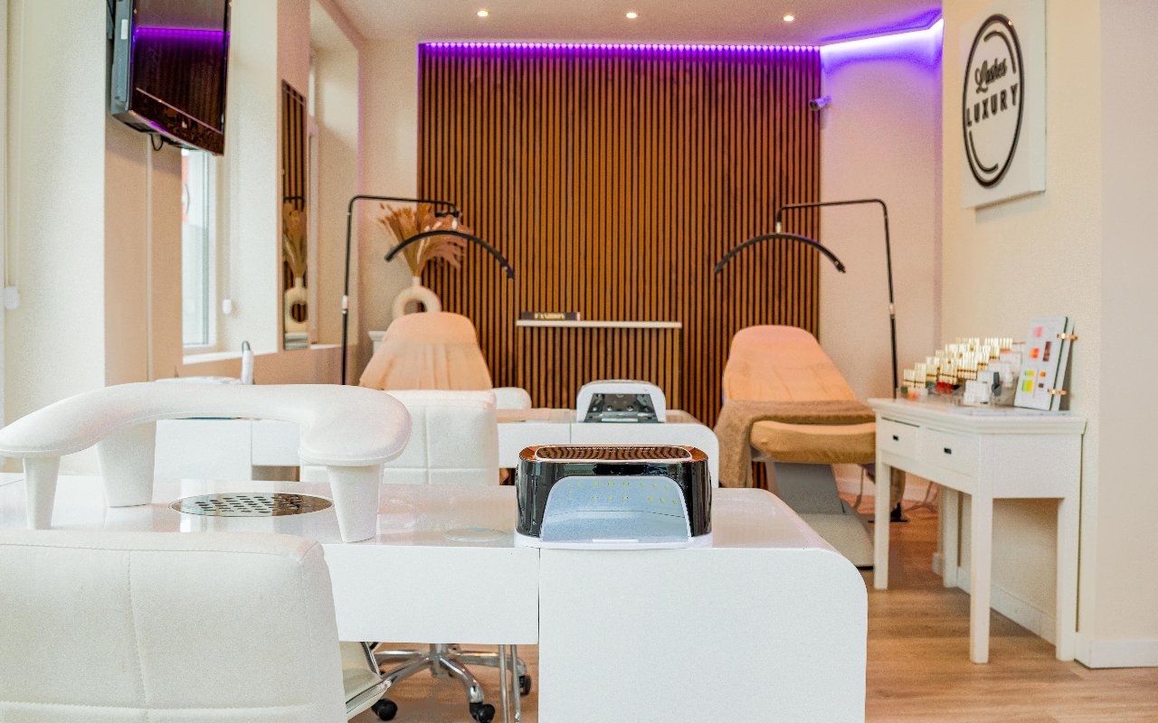 De salon van Lashes Luxury: behandelbedden, nageltafel en het wandbord met het logo