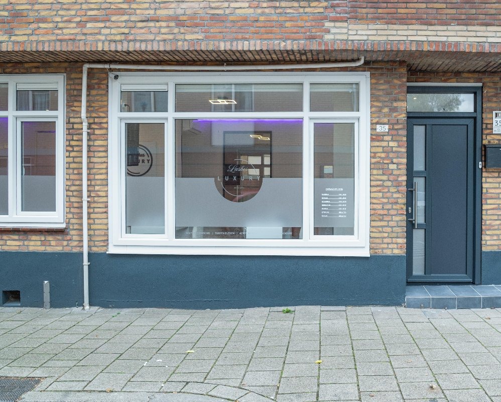 De salon van buiten: een bakstenen hoekpand met witte kozijnen en gematteerde ramen